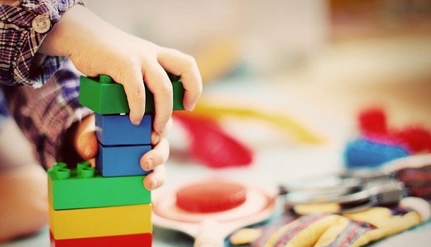 Bauen - Das Bild zeigt eine Kinderhand die einen Turm mit Bausteinen baut 